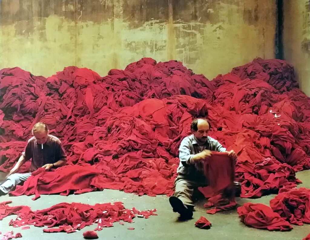 Scarti di tessuti rossi e due uomini seduti impegnati a sceglierli