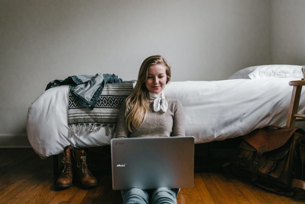 Femme assise par terre contre un lit avec un ordinateur portable sur les genoux